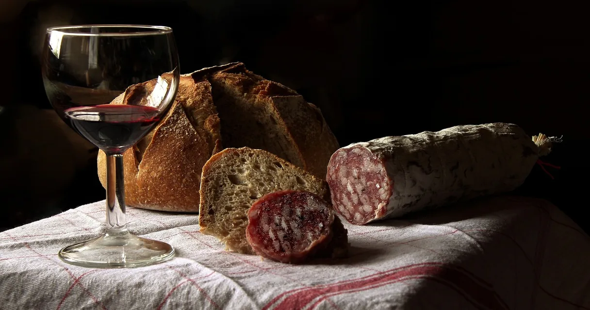 Taça de vinho tinto ao lado de pão e embutido sobre uma toalha de mesa, ilustrando como tirar mancha de vinho em roupa